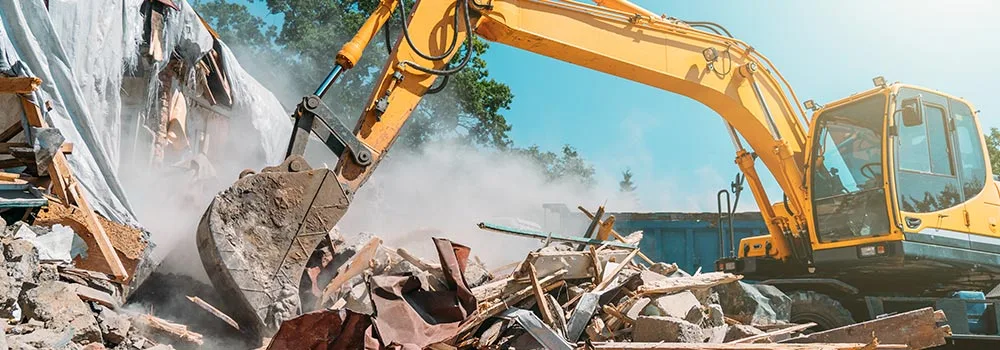 An excavator tears through a demolition site; every machine hour like this is real money that belongs on the job cost