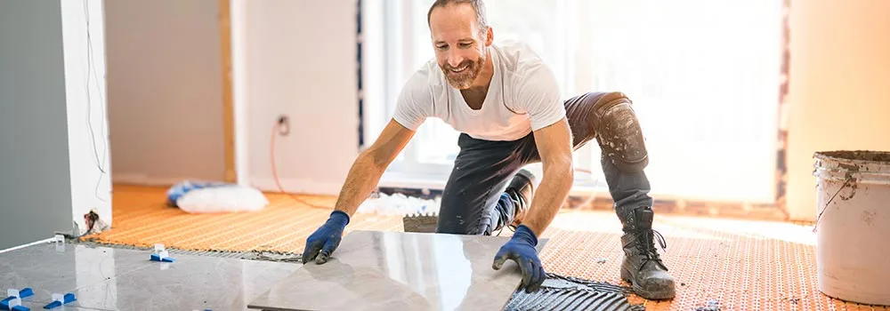 A tile setter lays large format tile late in a project; finish work is often done long before the held retainage is released