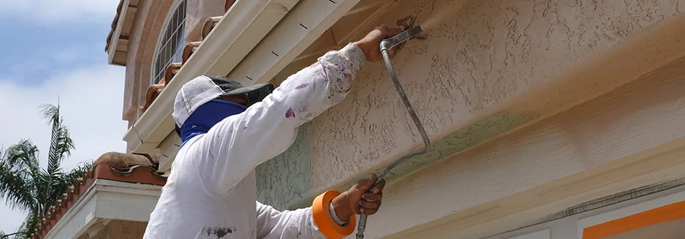 Painter rolling paint on a home exterior
