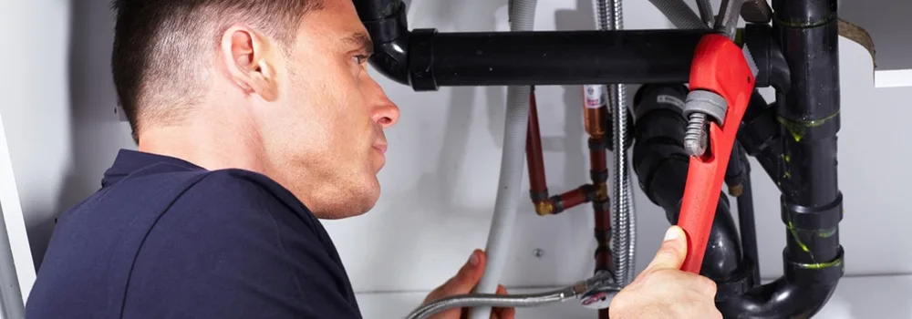 Plumbing contractor repairing pipes under a sink on a service call