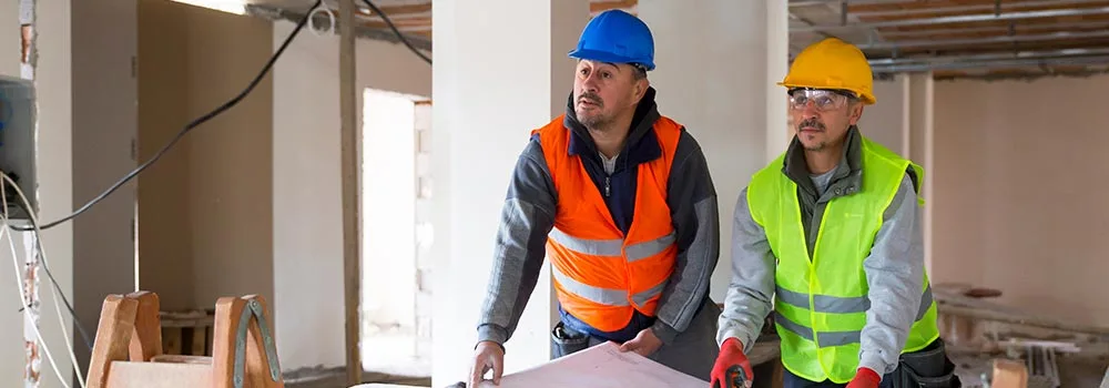 A contractor carries a laptop through an unfinished structure; when jobs and crews outgrow your notebook, it is time for real project tools